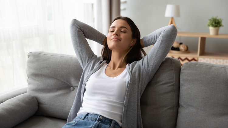 Nuori nainen istuu tyytyväisenä sohvalla, kun hän tuntee CBD:n vaikutukset, kuten stressin lievittämisen.