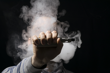 Vaporizing tobacco, hand holding vaporizer on black background